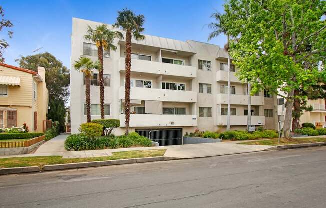 A modern white apartment building with palm trees in front.