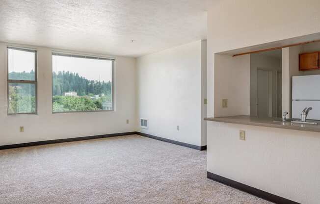 an empty living room with a kitchen and a large window