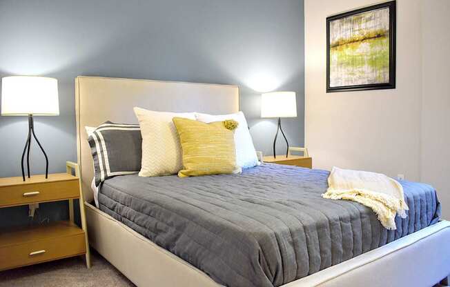 A bed with a grey cover and a white headboard with a yellow pillow and a white blanket.