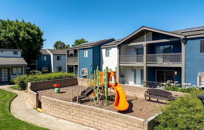 A playground area with a slide and a bench in front of apartment buildings.