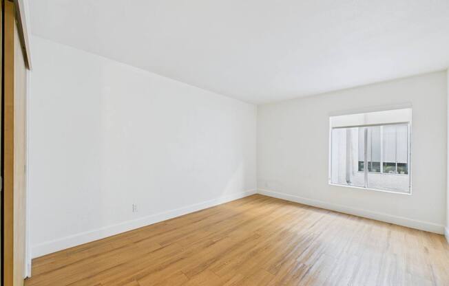 A room with wooden floors and a window with blinds.