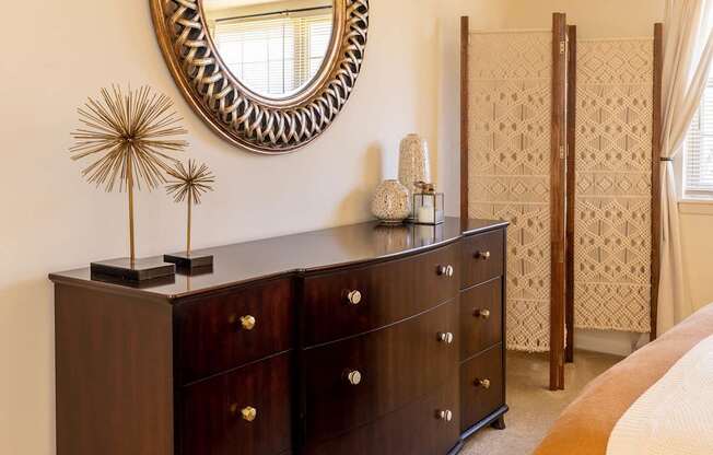 A bedroom with a large mirror and a dark brown dresser.