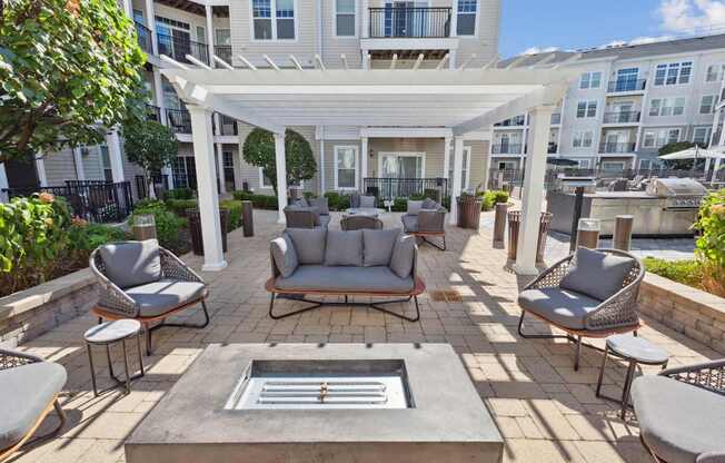 A patio with a white pergola and grey furniture.