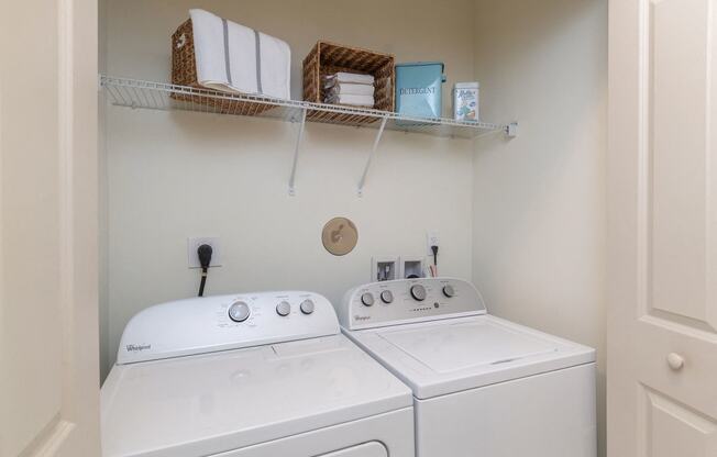 Open closet doors showing side-by-side full-sized washer and dryer with clothes rack above