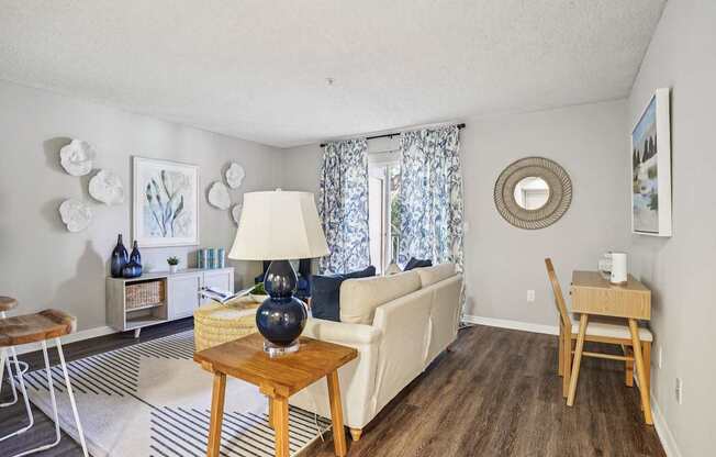 A living room with a white couch, a wooden coffee table, and a round mirror on the wall.