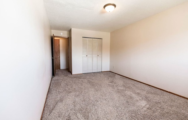 Grand Forks, ND Cherry Creek Apartments. A bedroom in unit 223 that has a window, white walls, a closet, and carpeted floors