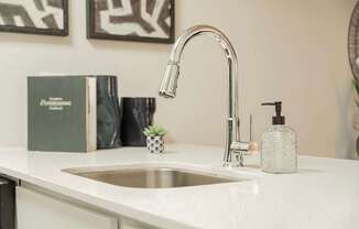 A modern kitchen sink with a chrome faucet and a bottle of soap.