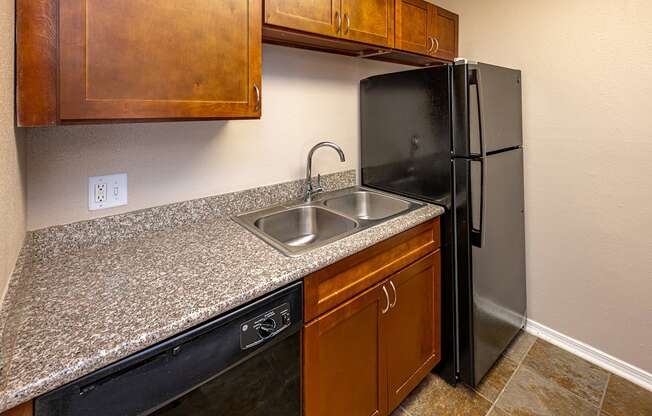 A kitchen with a black refrigerator and brown cabinets.