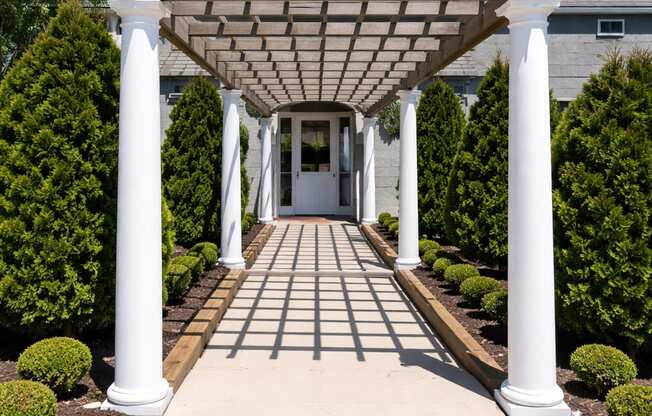 A white pillar covered walkway leads to a house.
