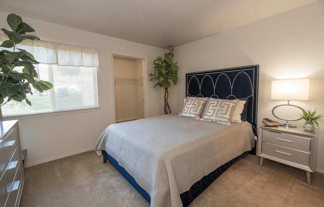A bedroom with a bed, nightstand, and a plant at Autumn Oaks Apartments, Roseville, CA, 95678