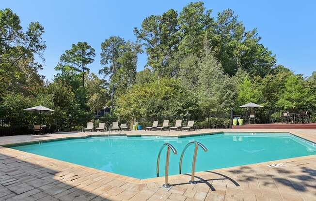 A swimming pool surrounded by trees and lounge chairs.
