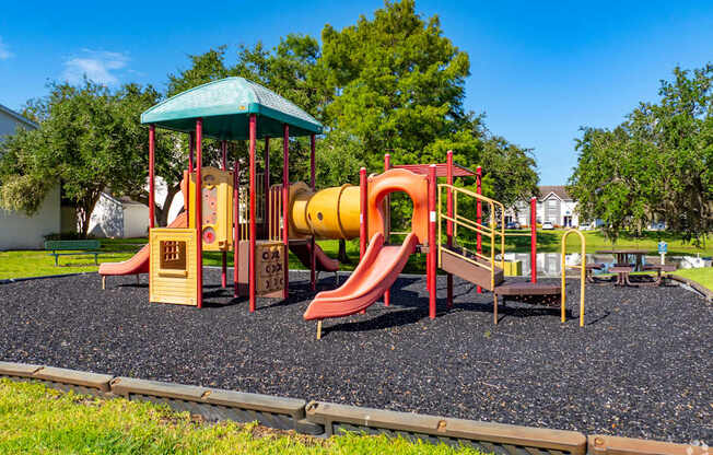 A playground with a red and yellow slide and a green roofed structure.