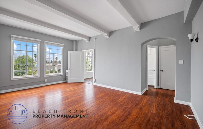 an empty living room with wood flooring and a door to a hallway with windows