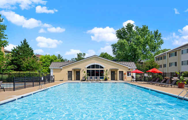 A large swimming pool in front of a building with a black fence and trees in the background.