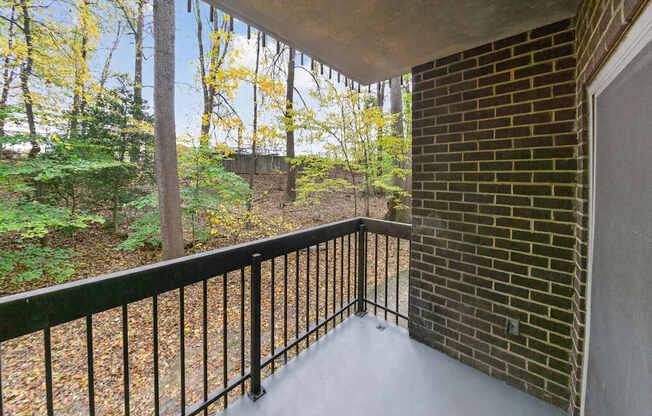 A balcony with a black railing and a view of trees and a hill.