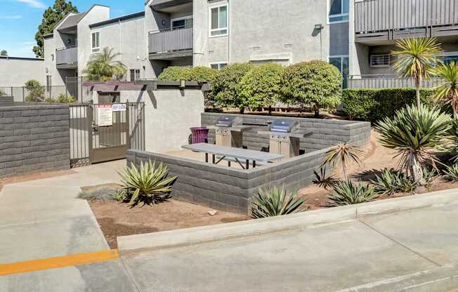A concrete patio with a brick wall and a small garden in front of apartment buildings.