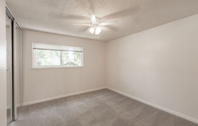 an empty bedroom with a ceiling fan and a window