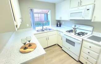 a kitchen with white cabinets and a white stove and a window