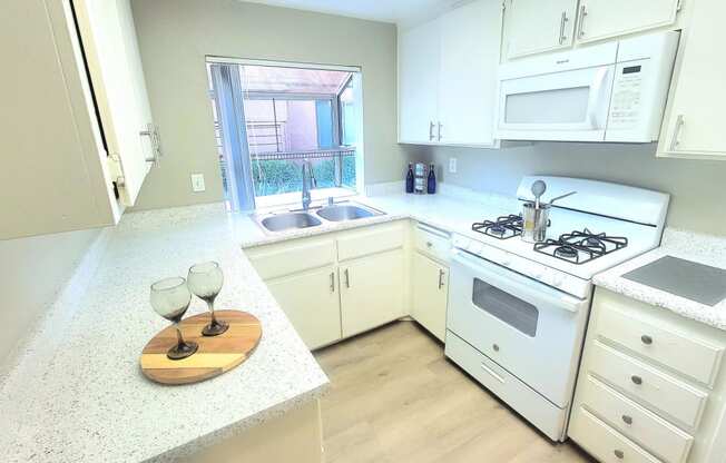 a kitchen with white cabinets and a white stove and a window