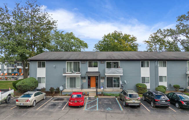 A parking lot in front of a grey apartment building with cars parked in designated spots.