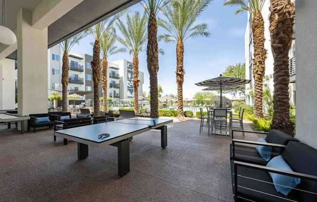 a patio with a ping pong table and chairs with palm trees in the background