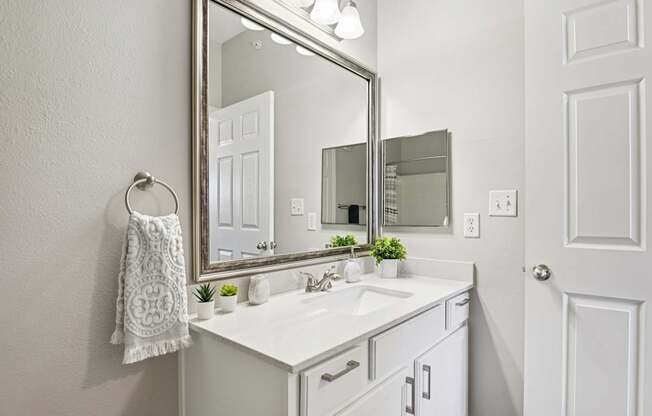 A white bathroom with a mirror, sink, and towel.