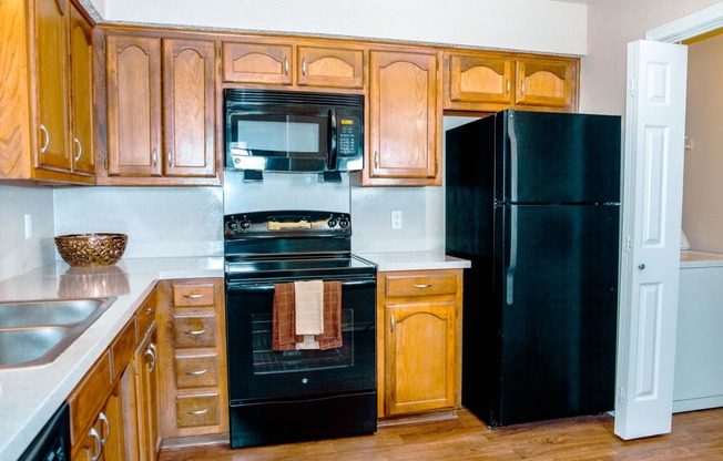 Kitchen with black appliances and wooden cabinets at Chisholm Place Apartments in Plano, TX