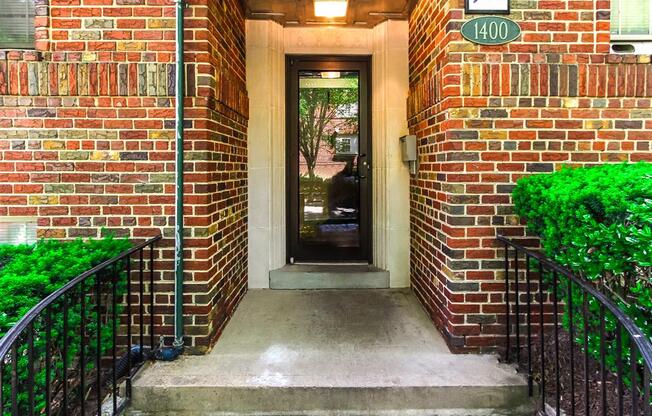 entrance of 1400 van buren apartments with lush landscaping, brick building and sidewalk