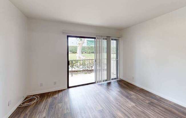 A room with wooden floors and white walls has a sliding glass door.