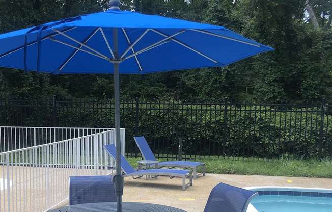A blue umbrella is next to a pool with a chair underneath it. at New Carrollton Woods, Riverdale, MD