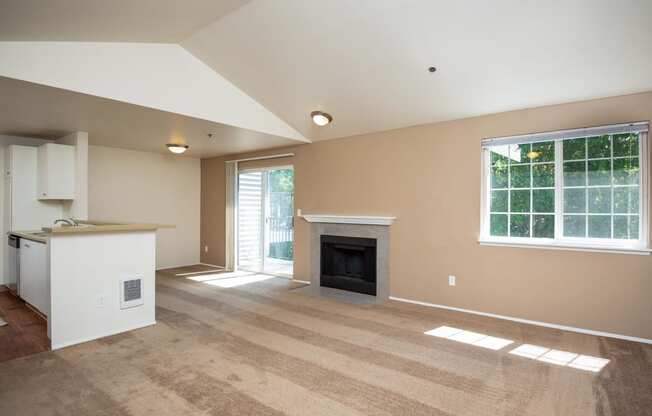 an empty living room with a fireplace and a kitchen