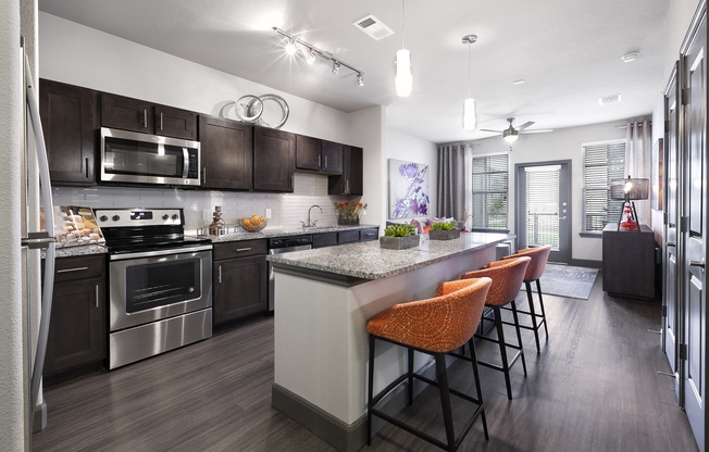 a kitchen with stainless steel appliances and a large island with chairs at North Creek, Texas, 78634