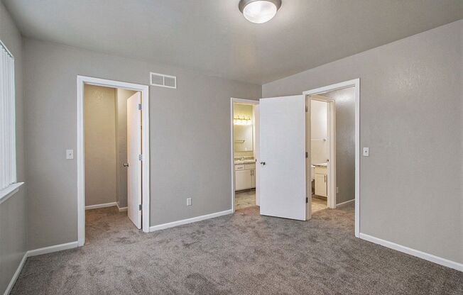 an empty room with a carpeted floor and doors to a bathroom