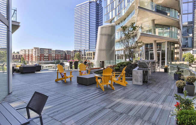A wooden deck with chairs and a table in the foreground with a cityscape in the background.