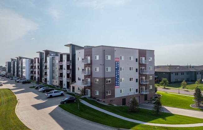 A row of apartment buildings with cars parked in front.