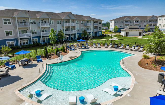 A large swimming pool surrounded by lounge chairs and umbrellas in a residential area.