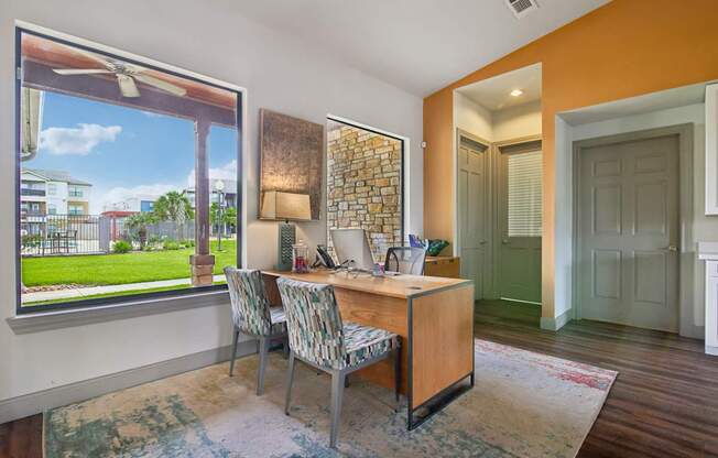 A room with a desk and chairs with a window overlooking a green lawn.