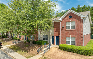 our apartments offer a spacious courtyard with trees and a brick building at Greens at Stonecreek, Lithonia, Georgia