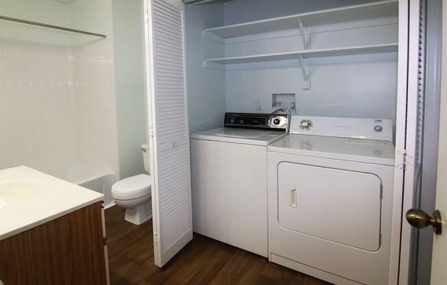 A white laundry machine is in a small, white closet.