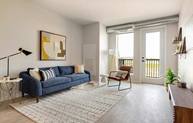 A living room with a blue couch, a chair, a coffee table, and a painting on the wall.