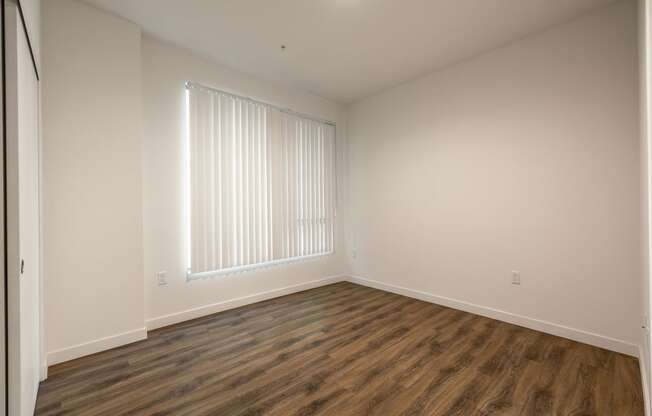 a bedroom with white walls and wood flooring and a window