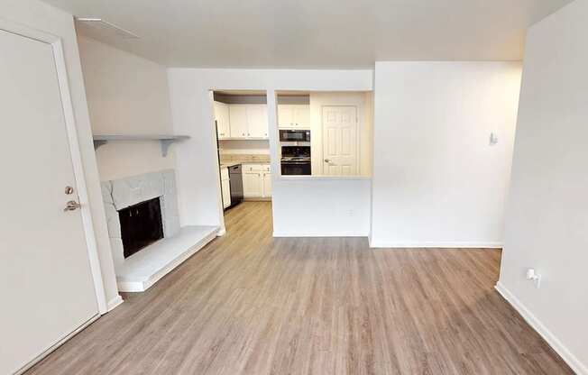 A room with a fireplace and a kitchen in the background.