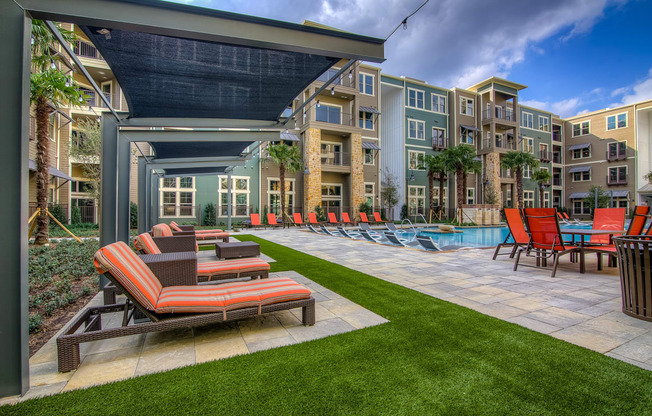 a patio with lounge chairs and a pool in front of an apartment building