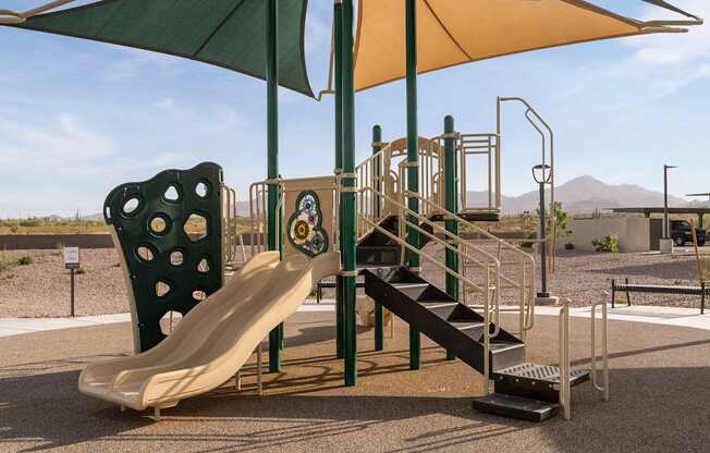 A playground with a yellow slide and a green umbrella.