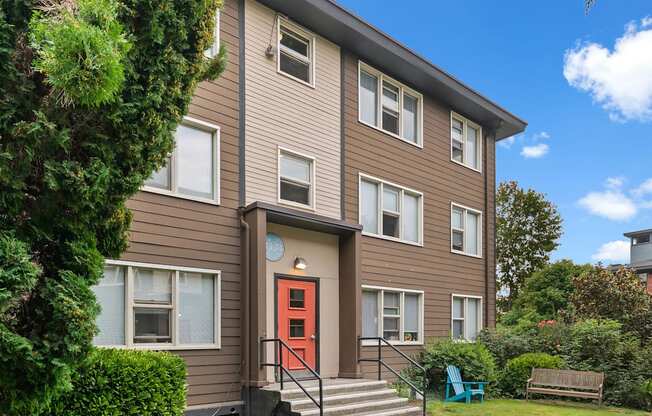 A brown house with a red door and a green chair in front.