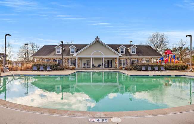 A large swimming pool in front of a building with a playground in the background.