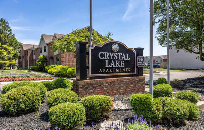 A sign for Crystal Lake Apartments is surrounded by bushes and flowers.