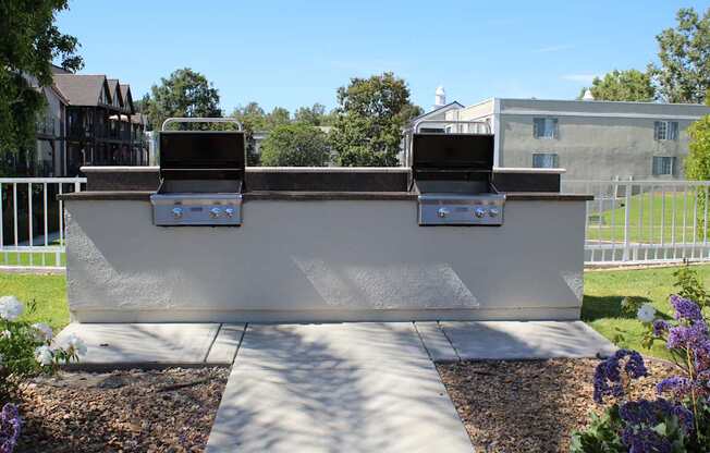 A white outdoor grill with two burners is in the middle of a gravel area.