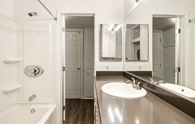 A white bathroom with a tub, sink, and mirror.