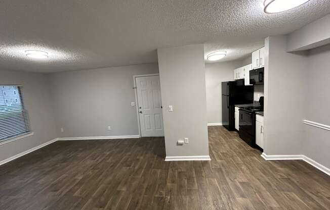 an empty living room with wood flooring and a kitchen